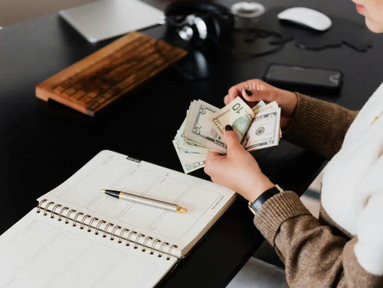 Person counting money at a desk with a planner, showcasing financial management and budgeting in a modern office setting.